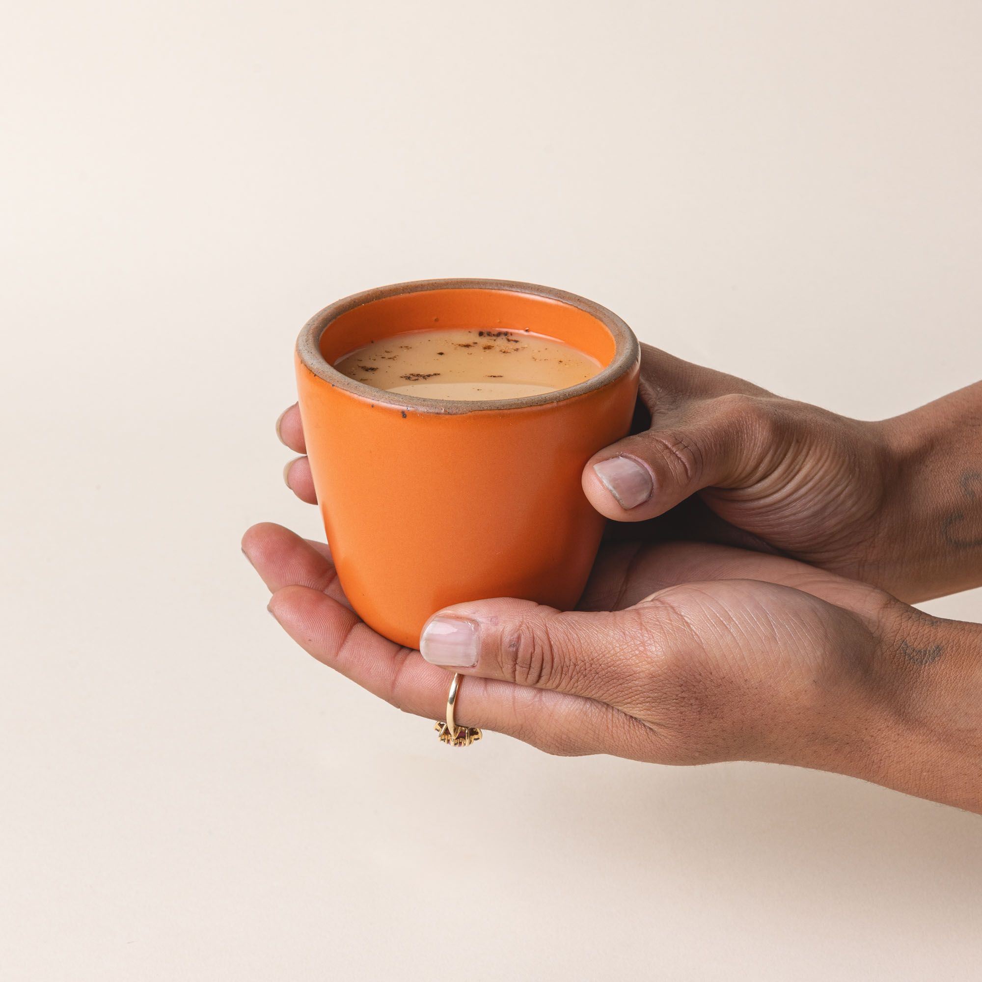 A hand holds a short cup that tapers out to get wider at the top in a bold orange color featuring iron speckles.