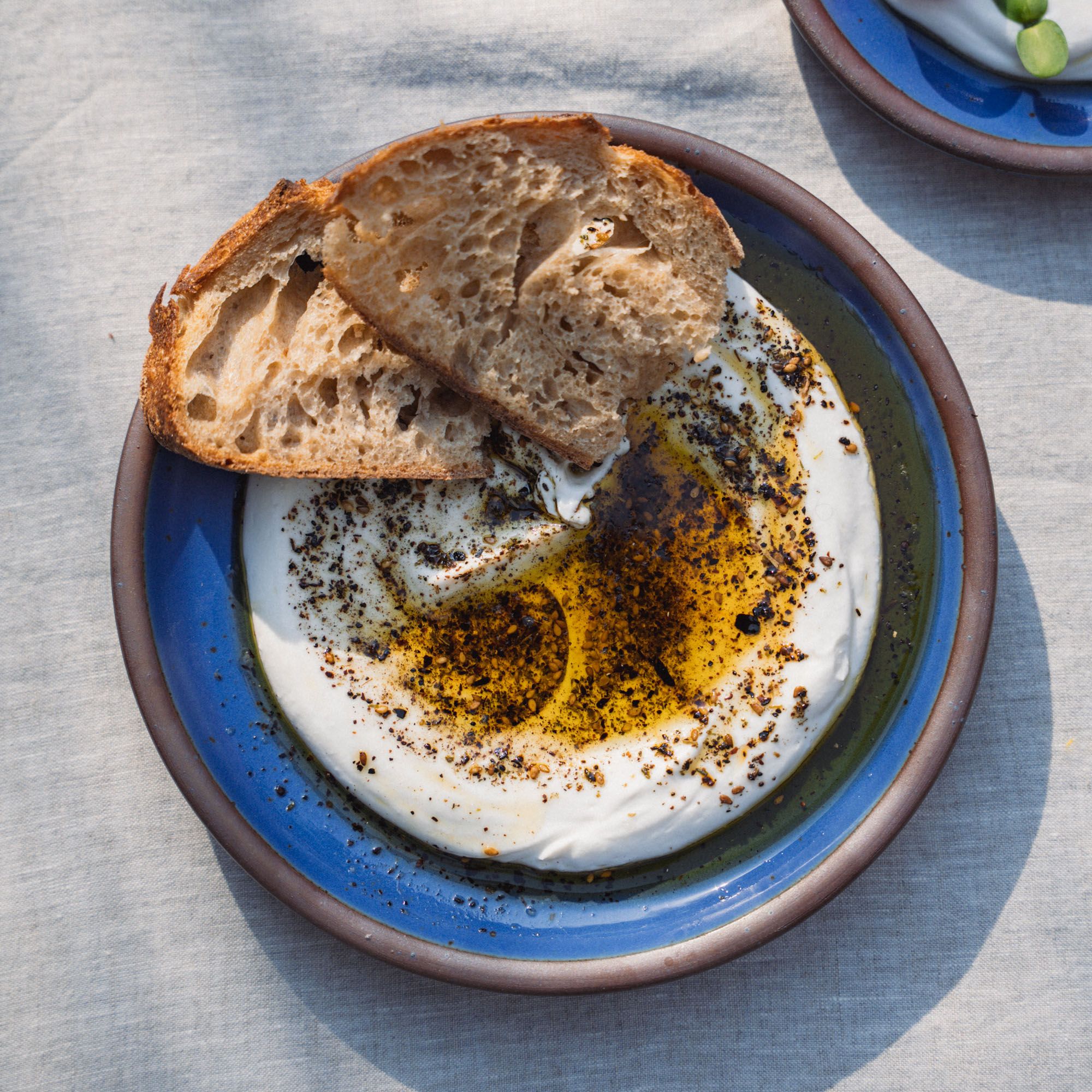 A medium sized plate in a cobalt blue color with a dip and olive oil, and 2 pieces of bread.
