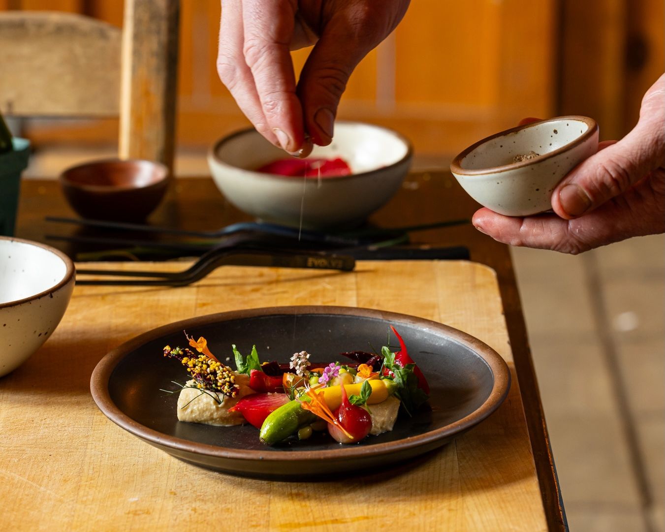 A hand sprinkles some garnish on a small beautiful ceramic plate of food