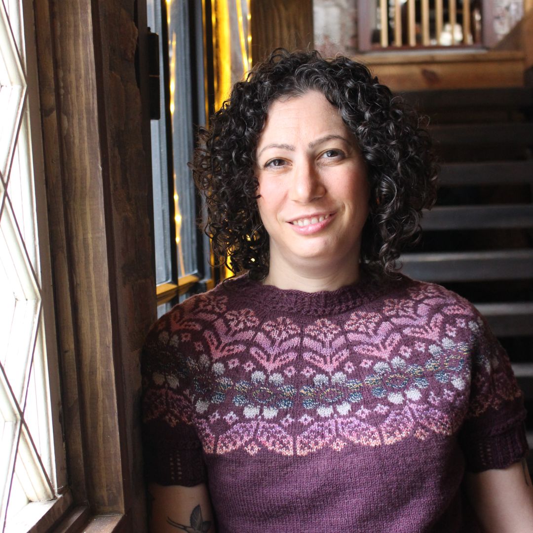 A person wearing a knitted purple shirt and smiling