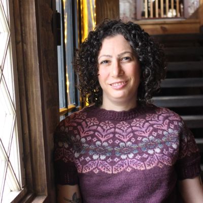 A person wearing a knitted purple shirt and smiling