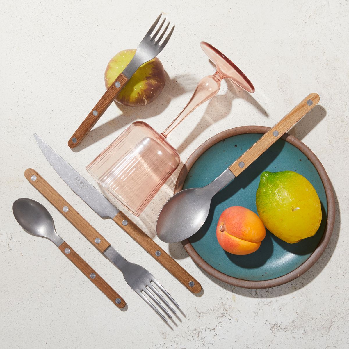 Silverware set with teak handles with pink wine glass, ceramic fruit and Secret Beach Cake Plate