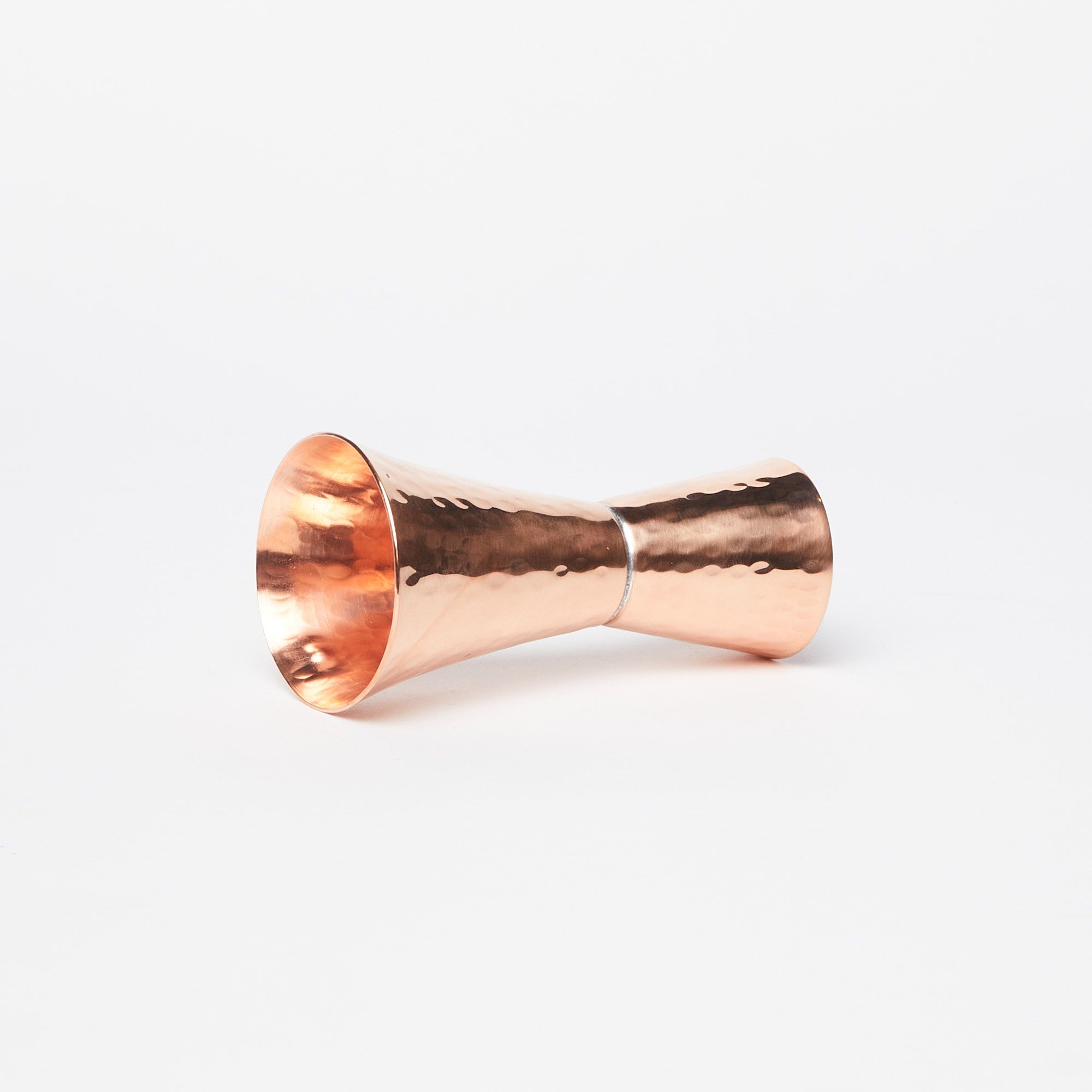 A double sided copper shot measurer laying on its side on a white background
