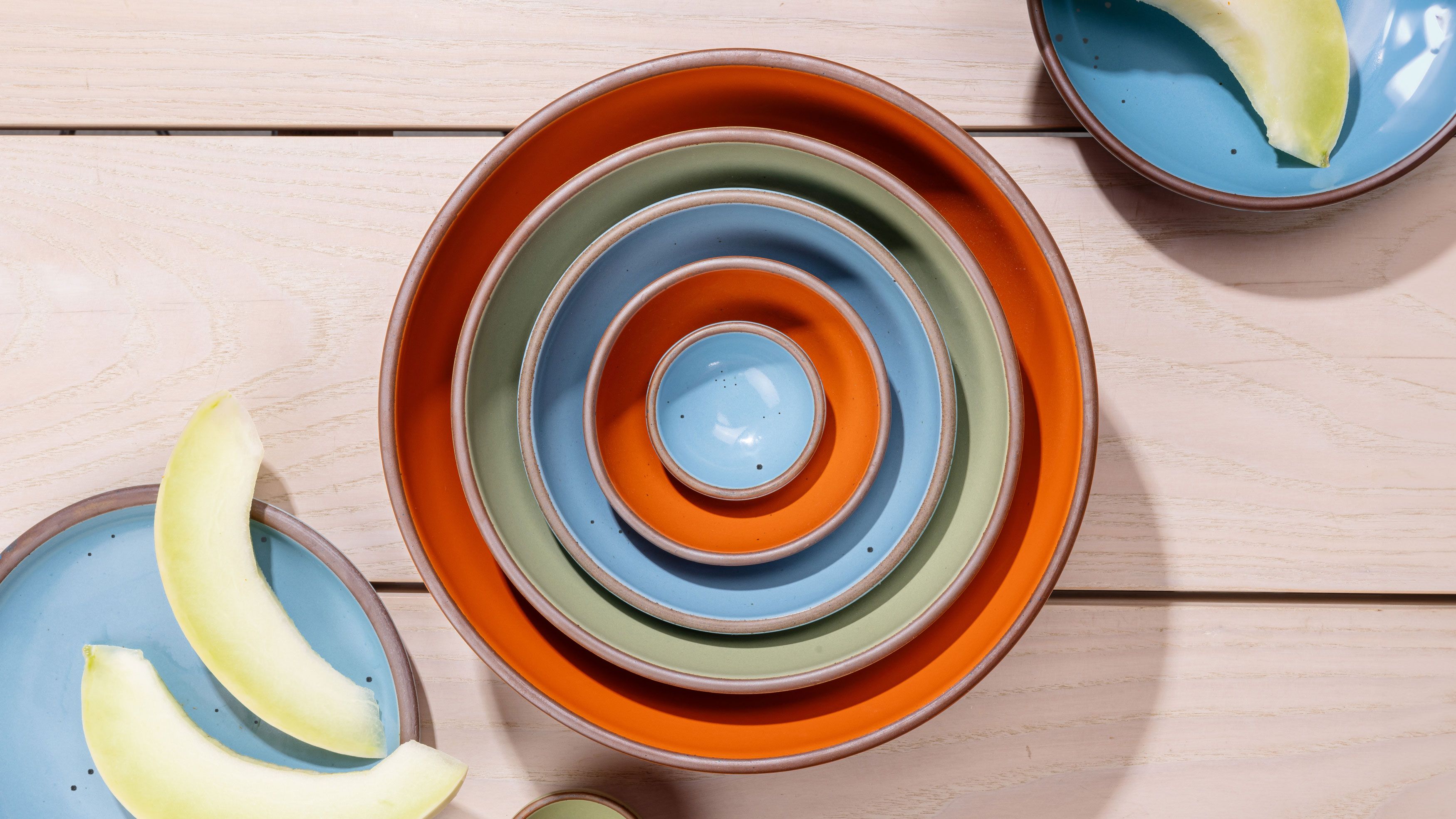 An overhead view of a nesting bowl set featuring 5 bowls - the largest being a kitchen mixing bowl, and the smallest being a tiny bowl for spices. Colors range from bold orange, calming sage green, and a robin's egg blue.