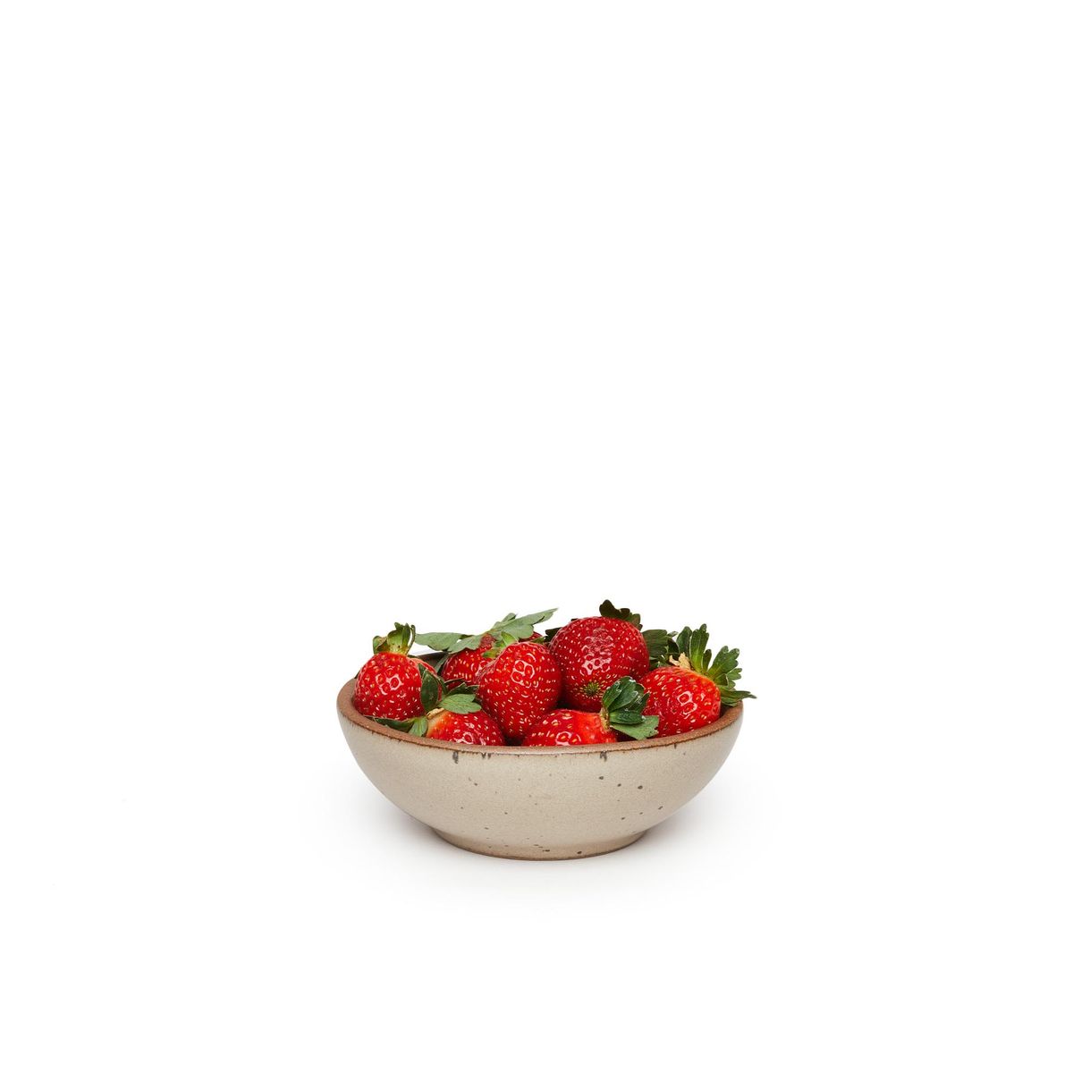 A small shallow ceramic bowl in a warm pale brown color featuring iron speckles and an unglazed rim, filled with strawberries