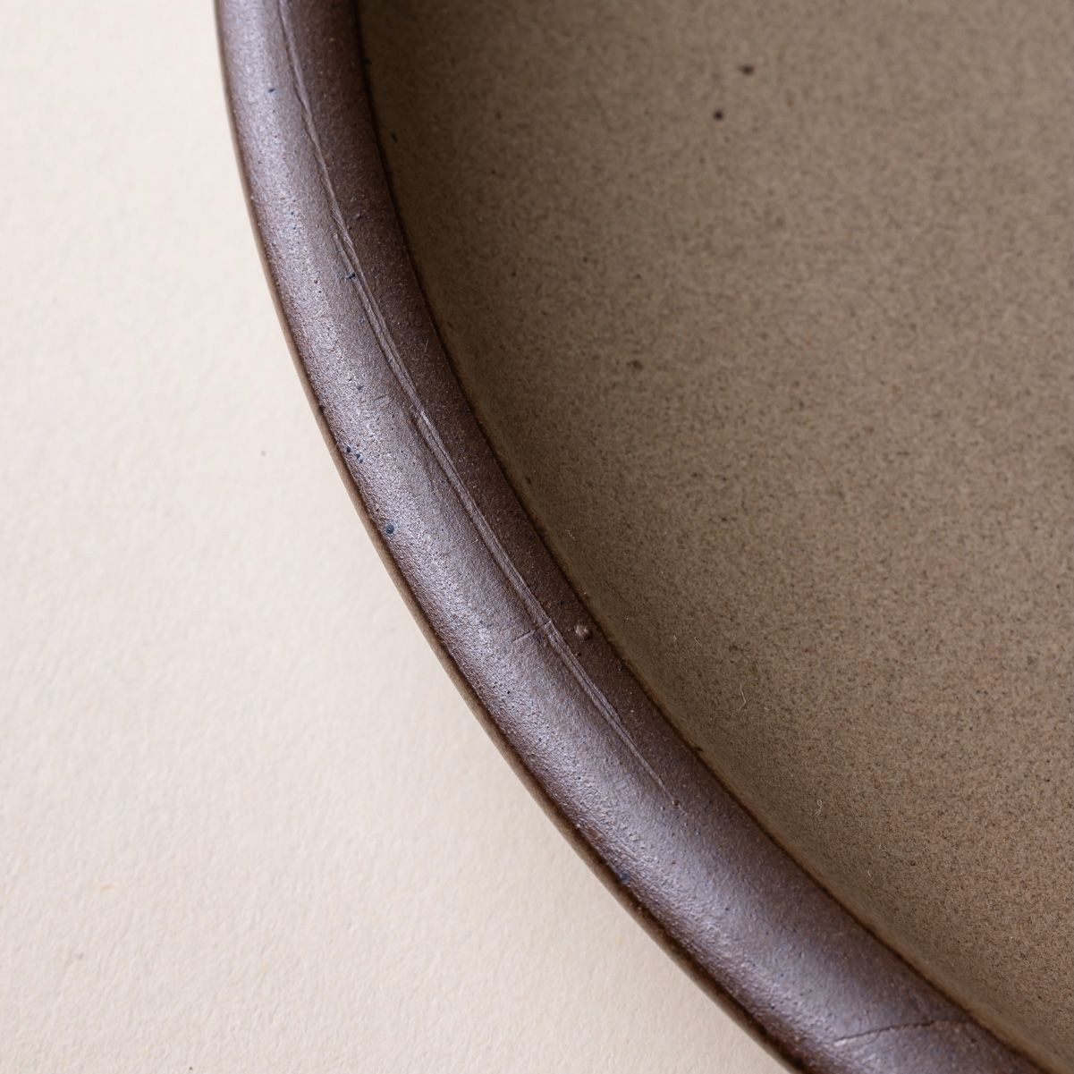 A closeup of the unglazed rim of a plate with a scratch running down the rim.