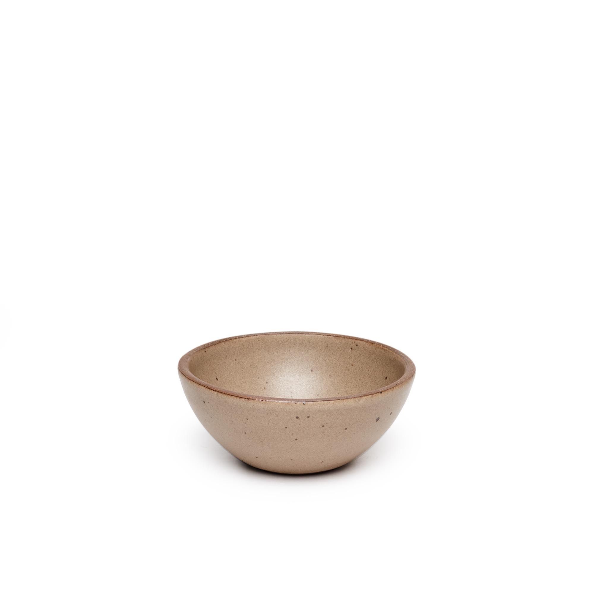 A small dessert sized rounded ceramic bowl in a warm pale brown color featuring iron speckles and an unglazed rim