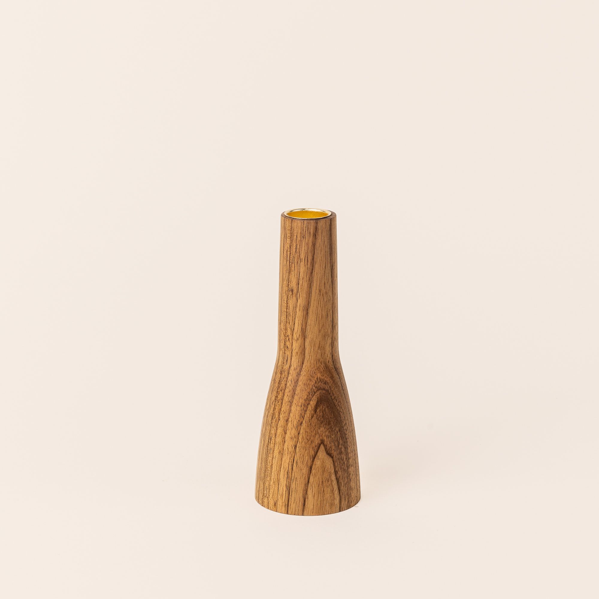 A butternut wood candle holder that is narrow shaped with a wider base on the bottom half and a thinner cylinder on the top half. On top is a a gold carved circle to hold the candle