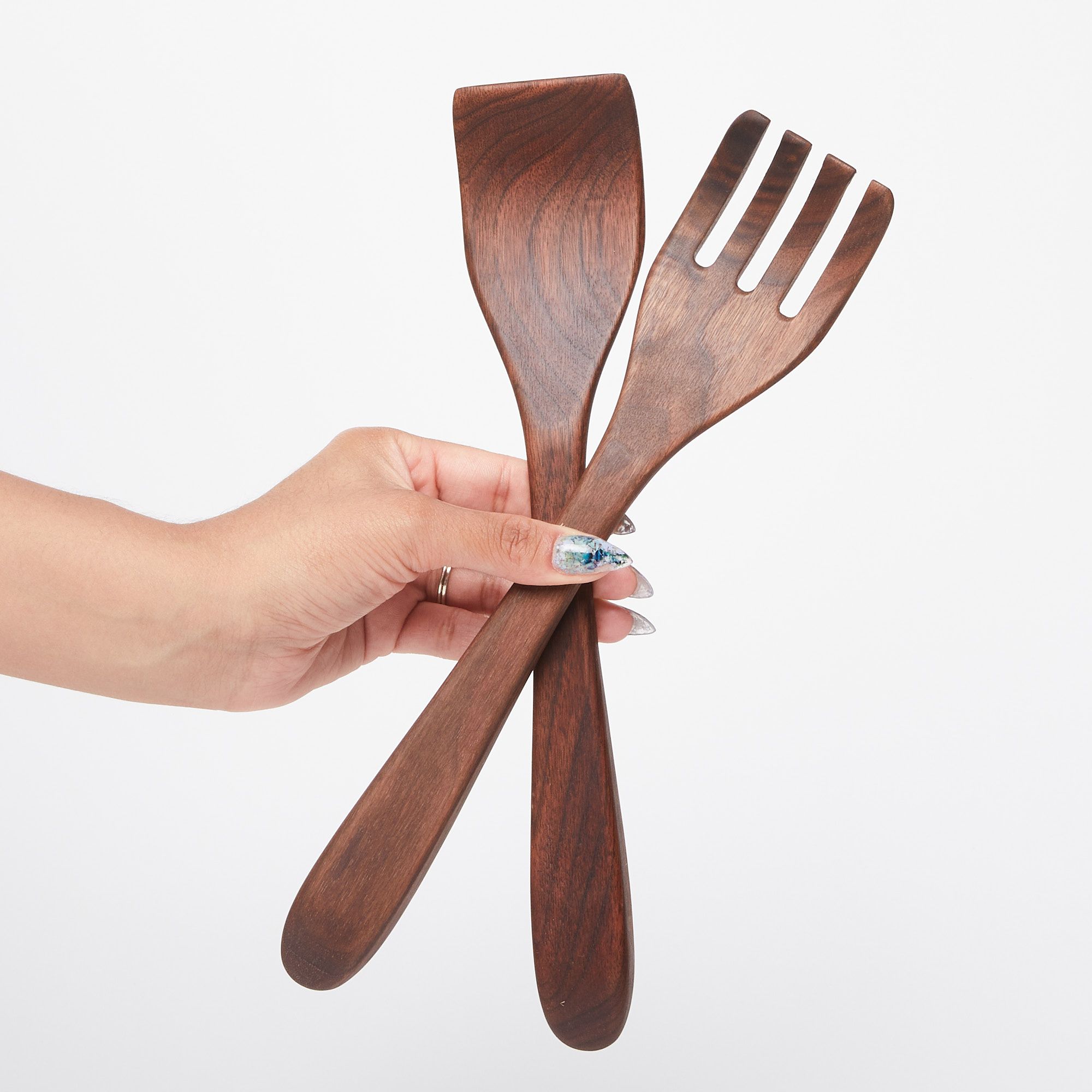 Hand holding a pair of long black walnut wood serving utensils