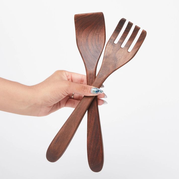 Hand holding a pair of long black walnut wood serving utensils