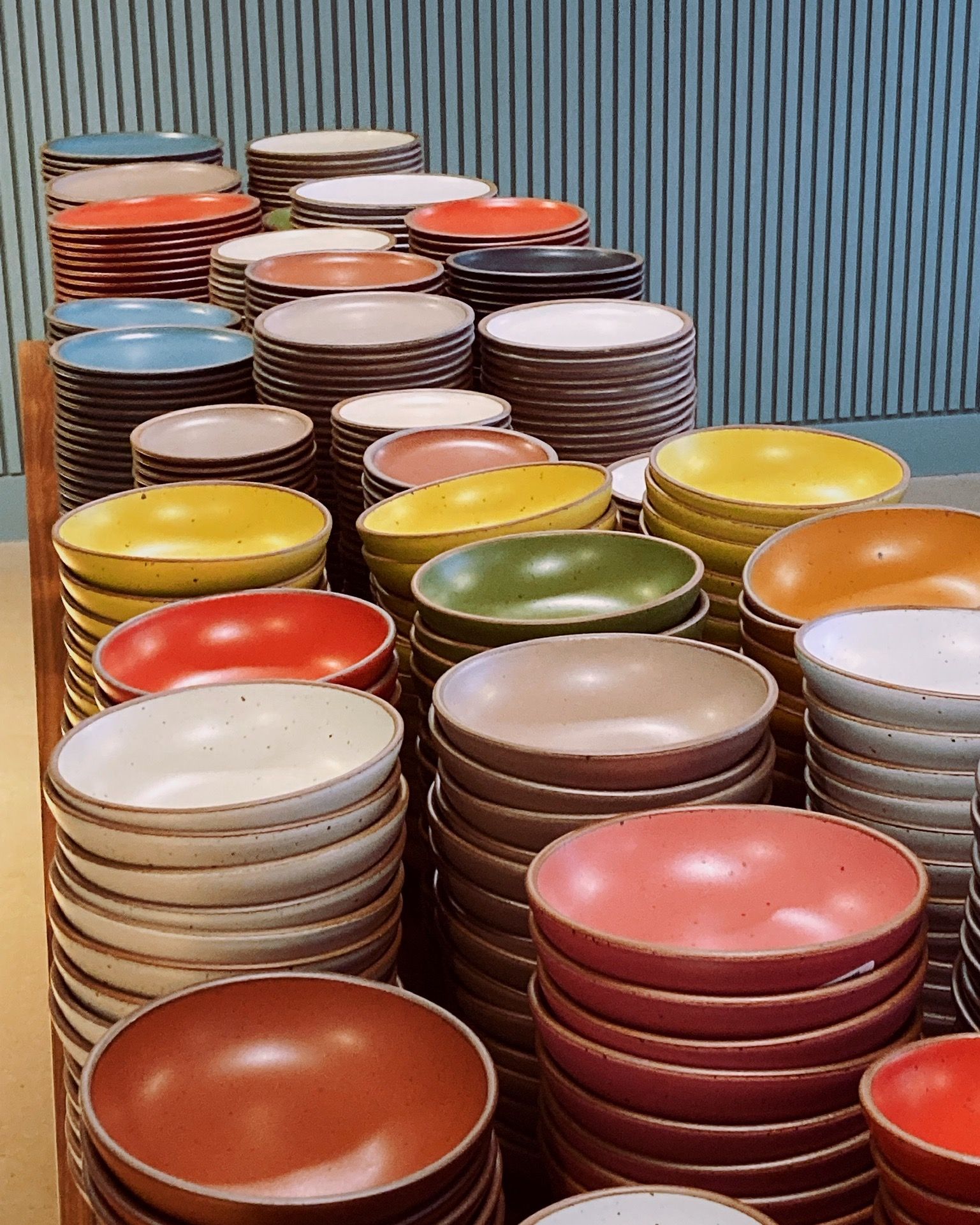 On a table, there are large stacks of ceramic bowls in all different colors of the rainbow