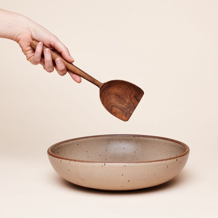 Hand holding a walnut scoop over an East Fork Everyday Bowl in Morel