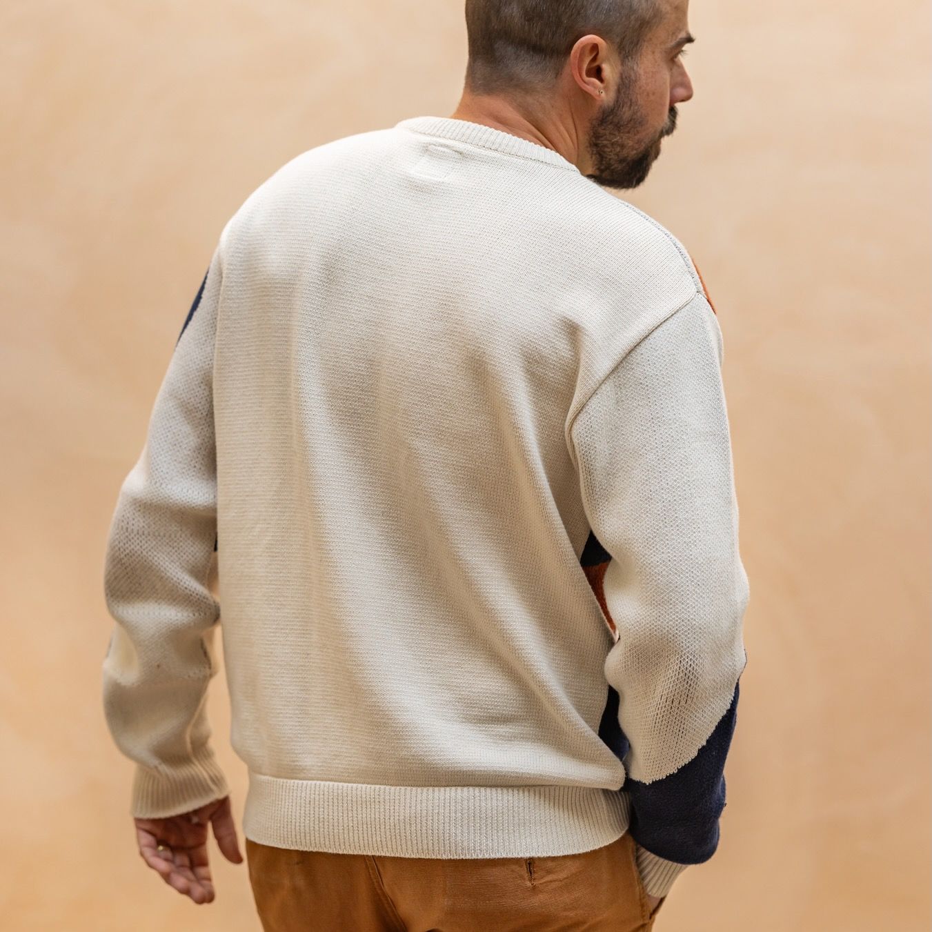 Alex shows off the back of a sweater in cream with some navy blocks of color on the sleeves.