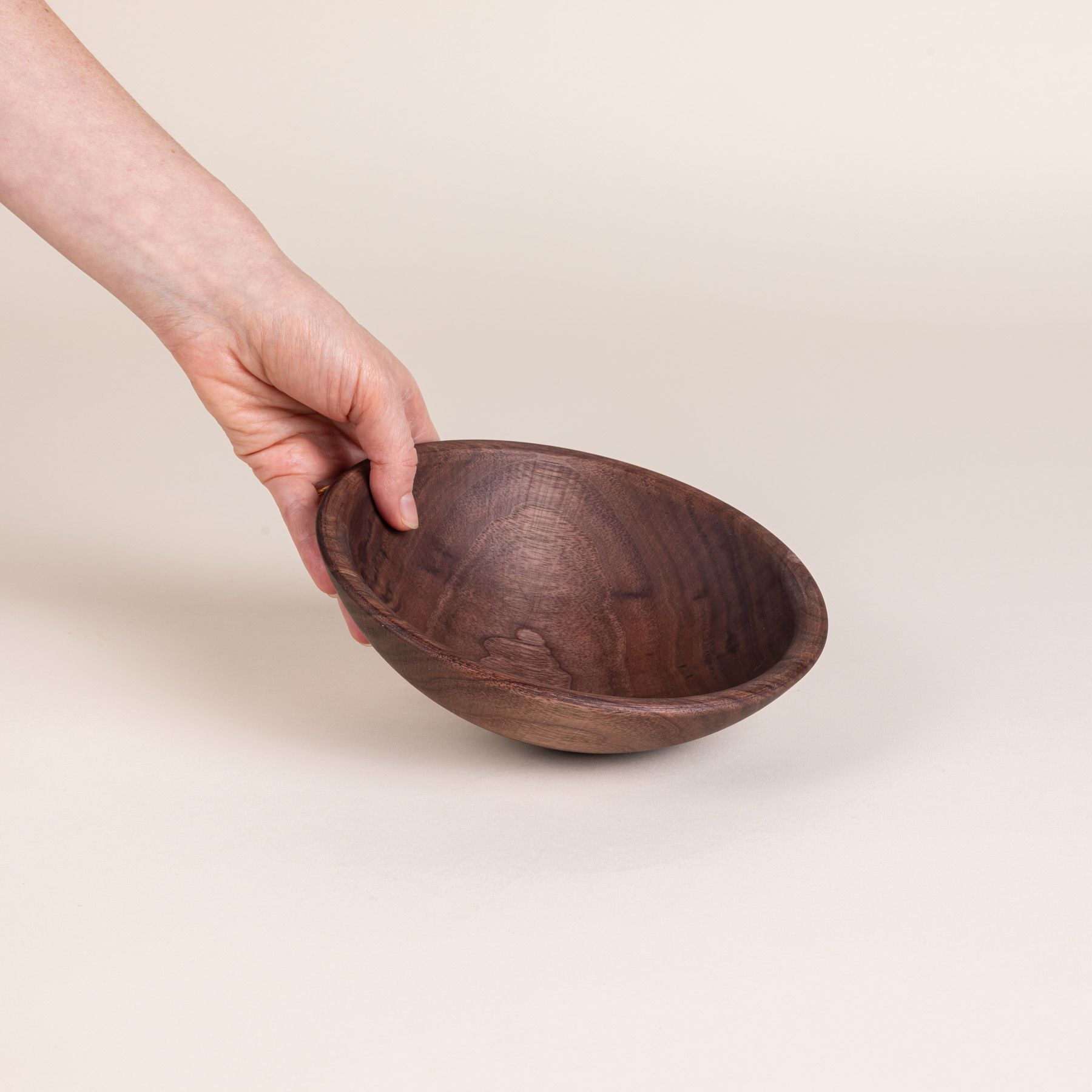 A hand holds out a small walnut wood bowl