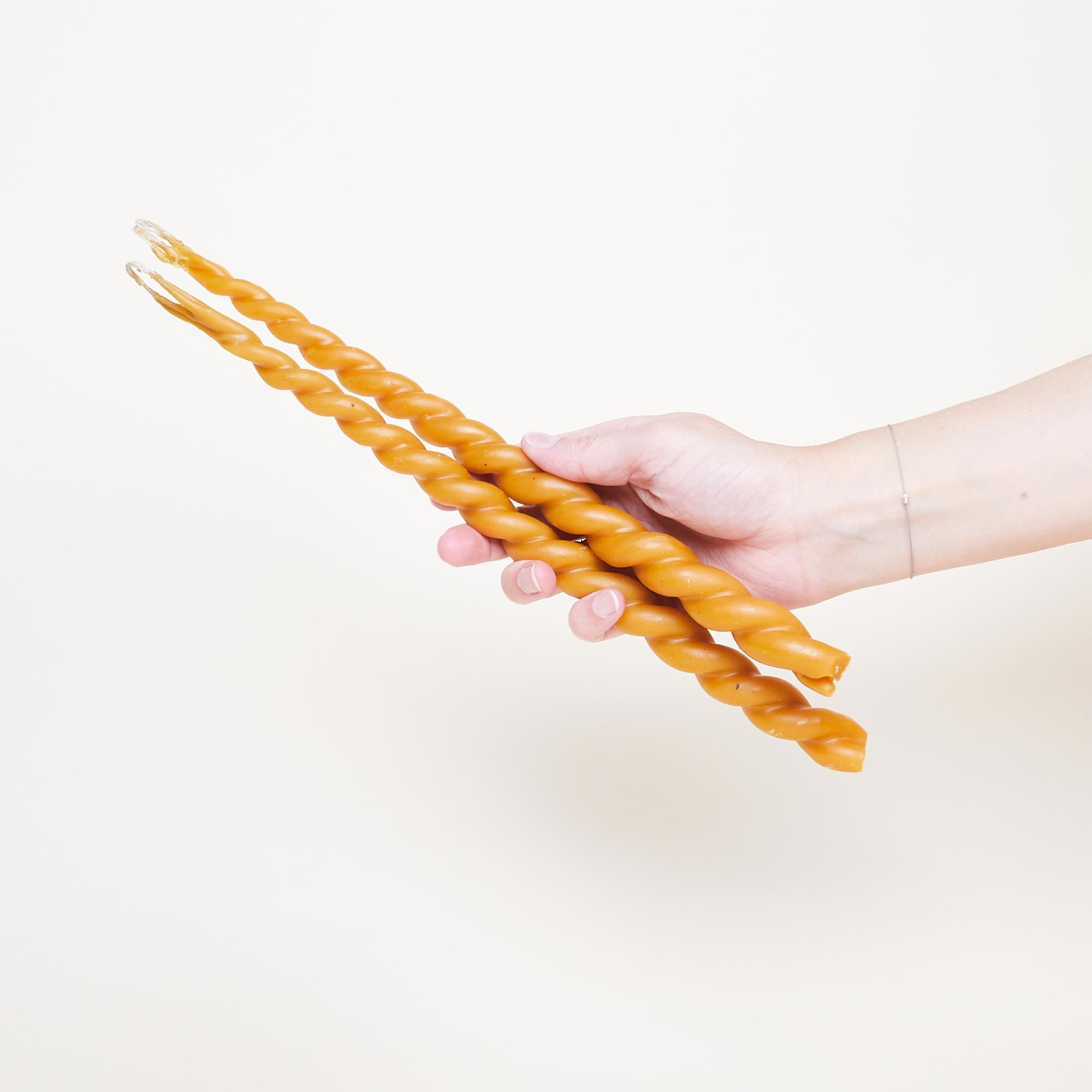 In a hand, two long golden yellow candles made from two pieces of wax that were twisted around each other