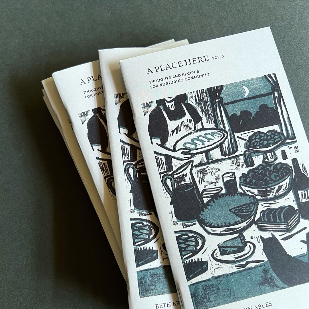 A stack of zines with an illustration of a figure hosting a large dinner, with writing at the top that reads "A Place Here"