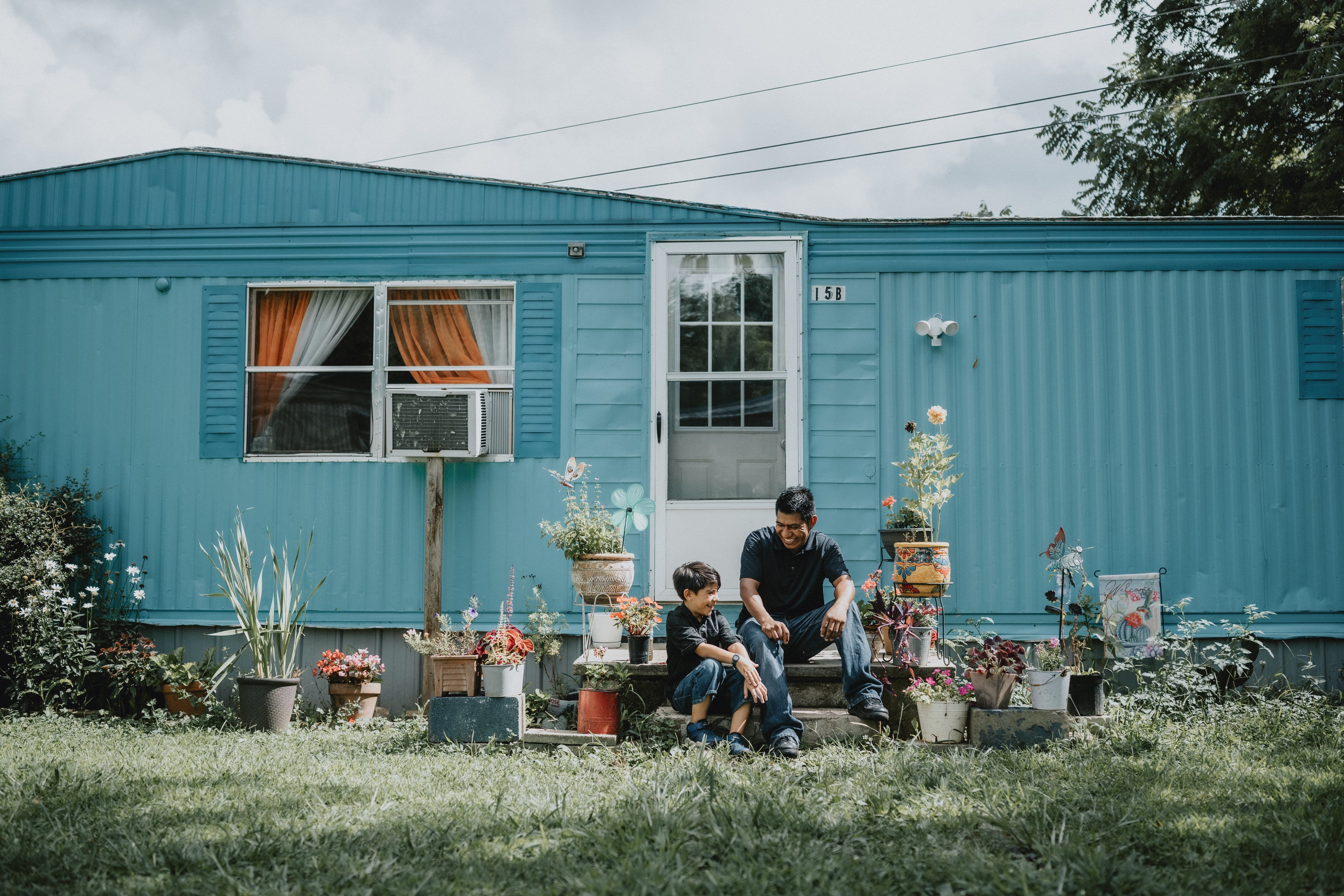 An adult and child sit outside of the entry door to their home that is painted blue