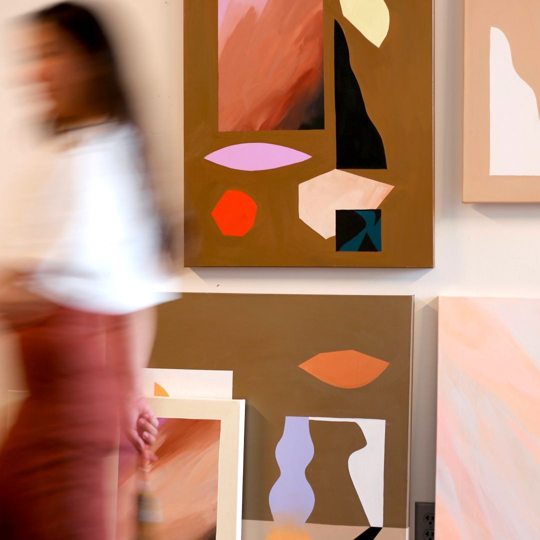 Large art pieces made with collage on a wall and a person walking by them.
