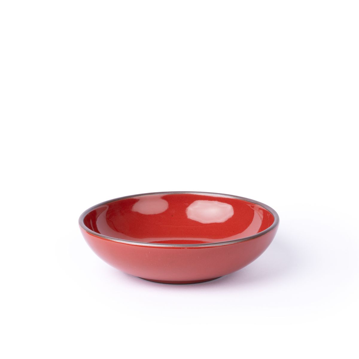 A dinner-sized shallow ceramic bowl in a glossy red color featuring iron speckles and an unglazed rim