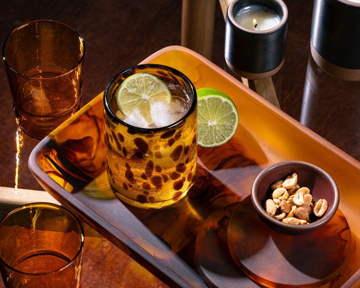 A tortoiseshell drinking glass filled with a drink and sitting on a tortoiseshell tray with coasters