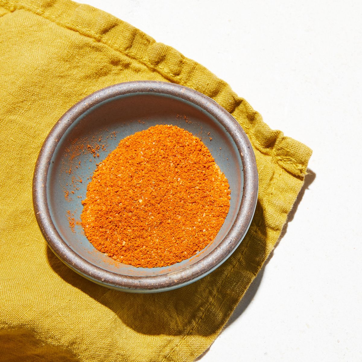 Small bowl full of a vibrant orange spice sitting atop a yellow fabric napkin