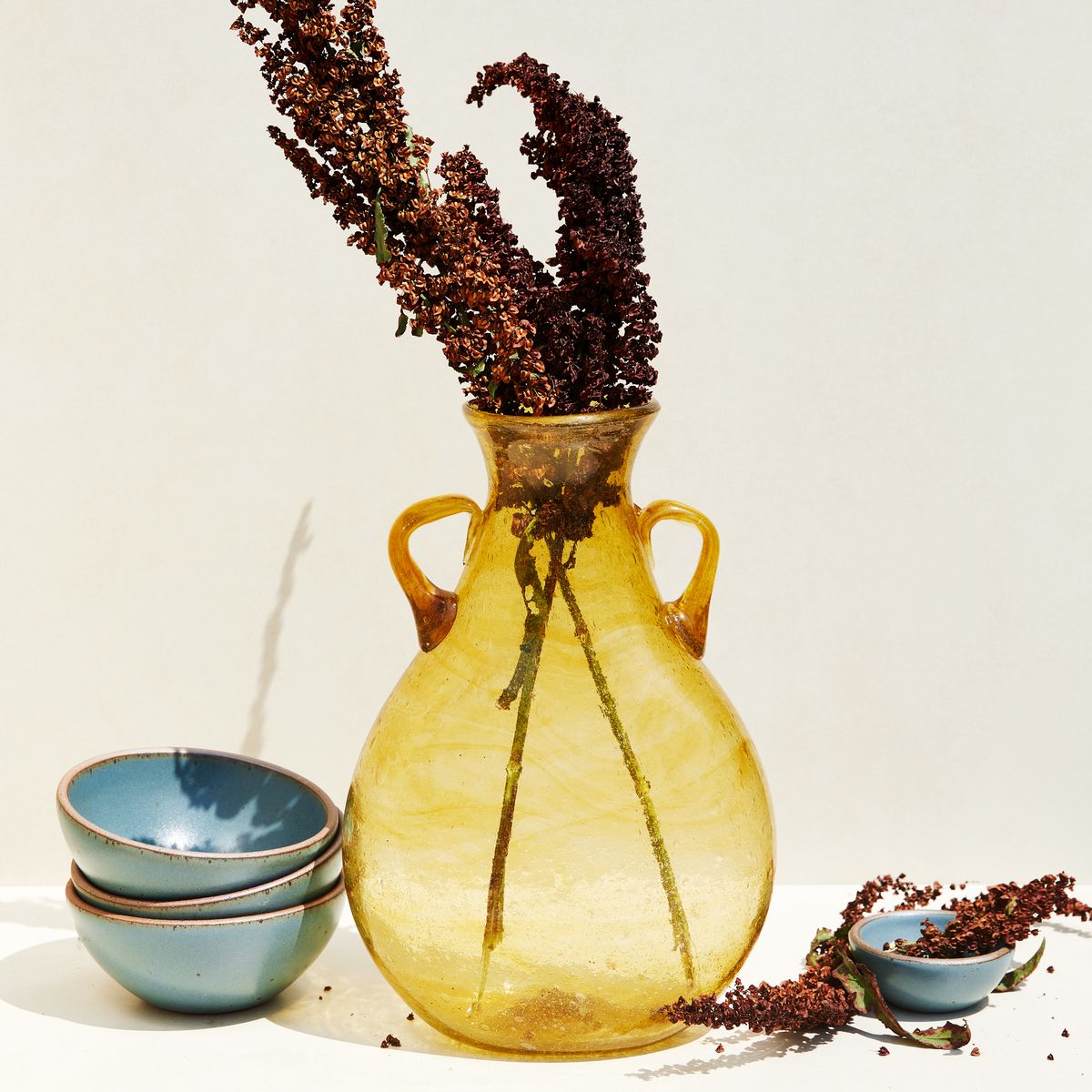 translucent yellow vase, narrowing at the top with two small handles filled with branches, sitting next to bowls