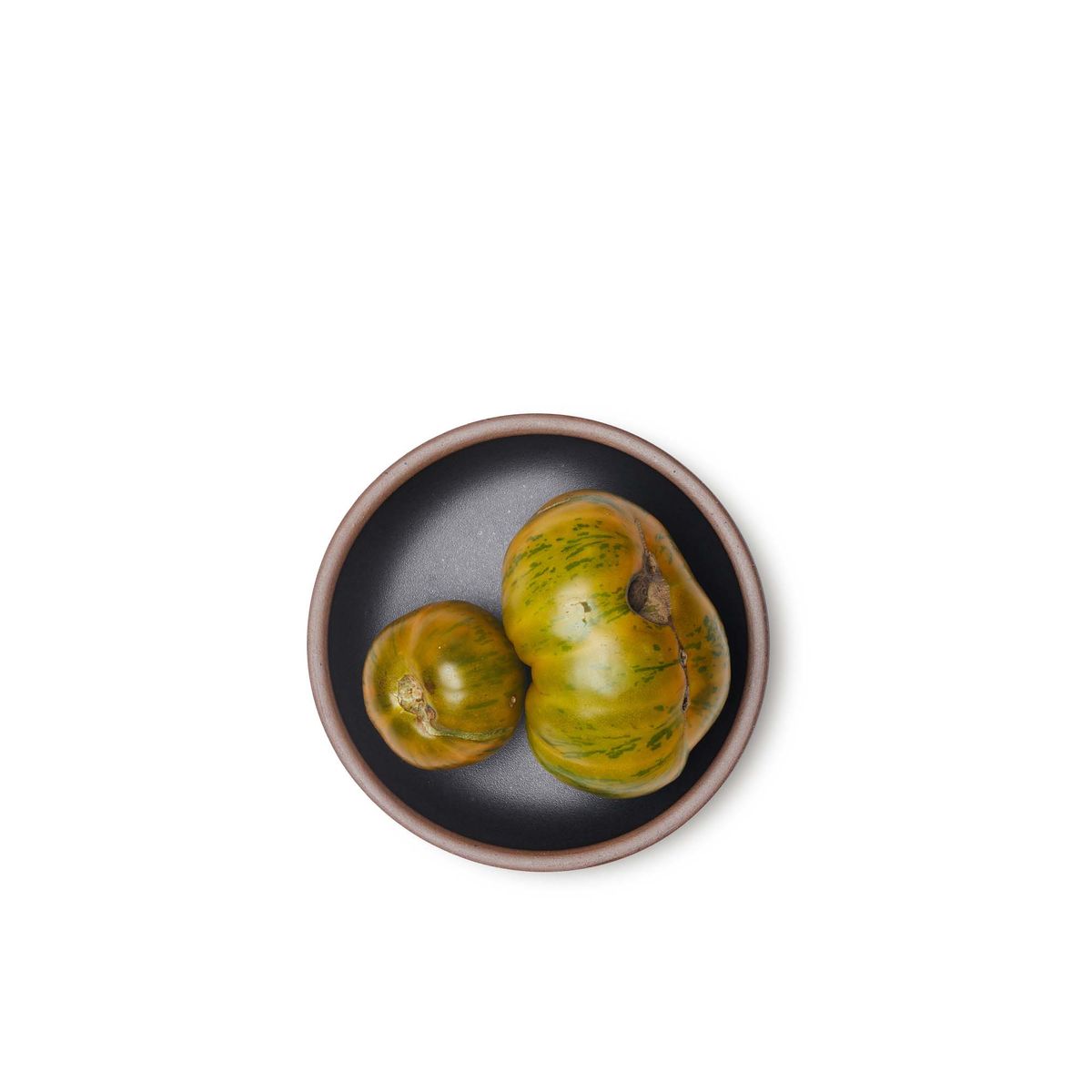 Tomatoes on a dessert sized ceramic plate in a graphite black color featuring iron speckles and an unglazed rim.