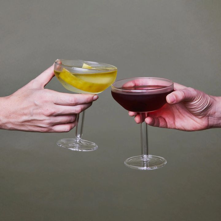 Two Hands Cheers Martini Coupes, one filled with a clear martini with a lemon twist, the other with wine