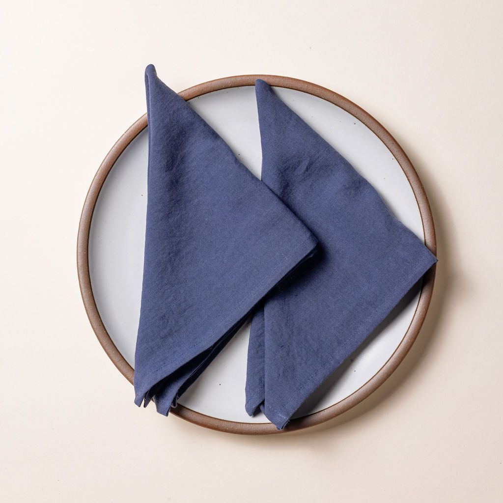 Two muted blue linen napkins folded into triangles on a white ceramic plate.