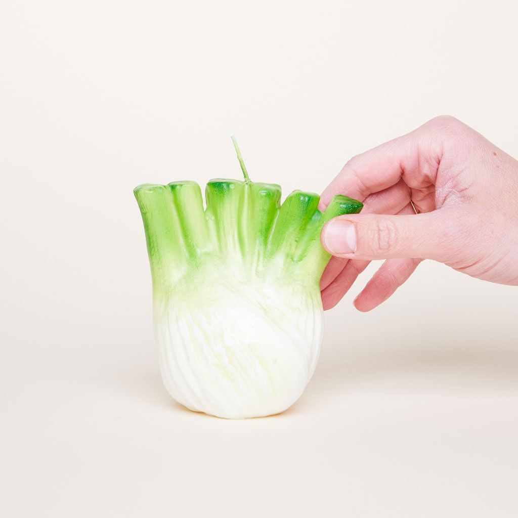 A hand touches a candle that in inspired by a fennel bulb.