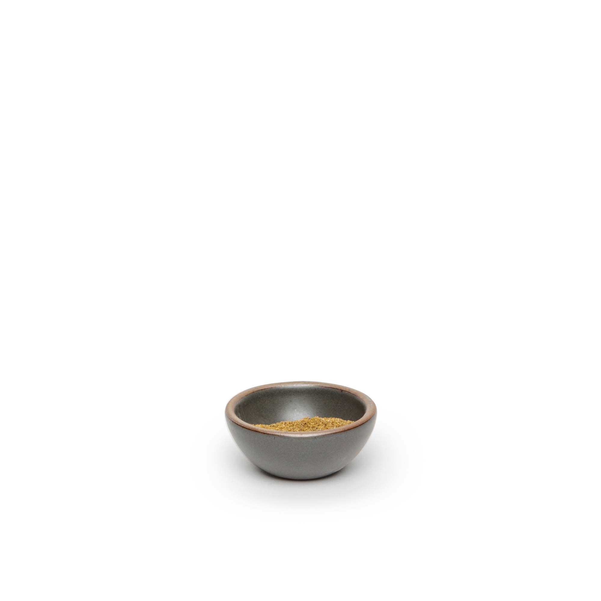 A tiny rounded ceramic bowl in a cool, medium grey color featuring iron speckles and an unglazed rim, filled with seasoning