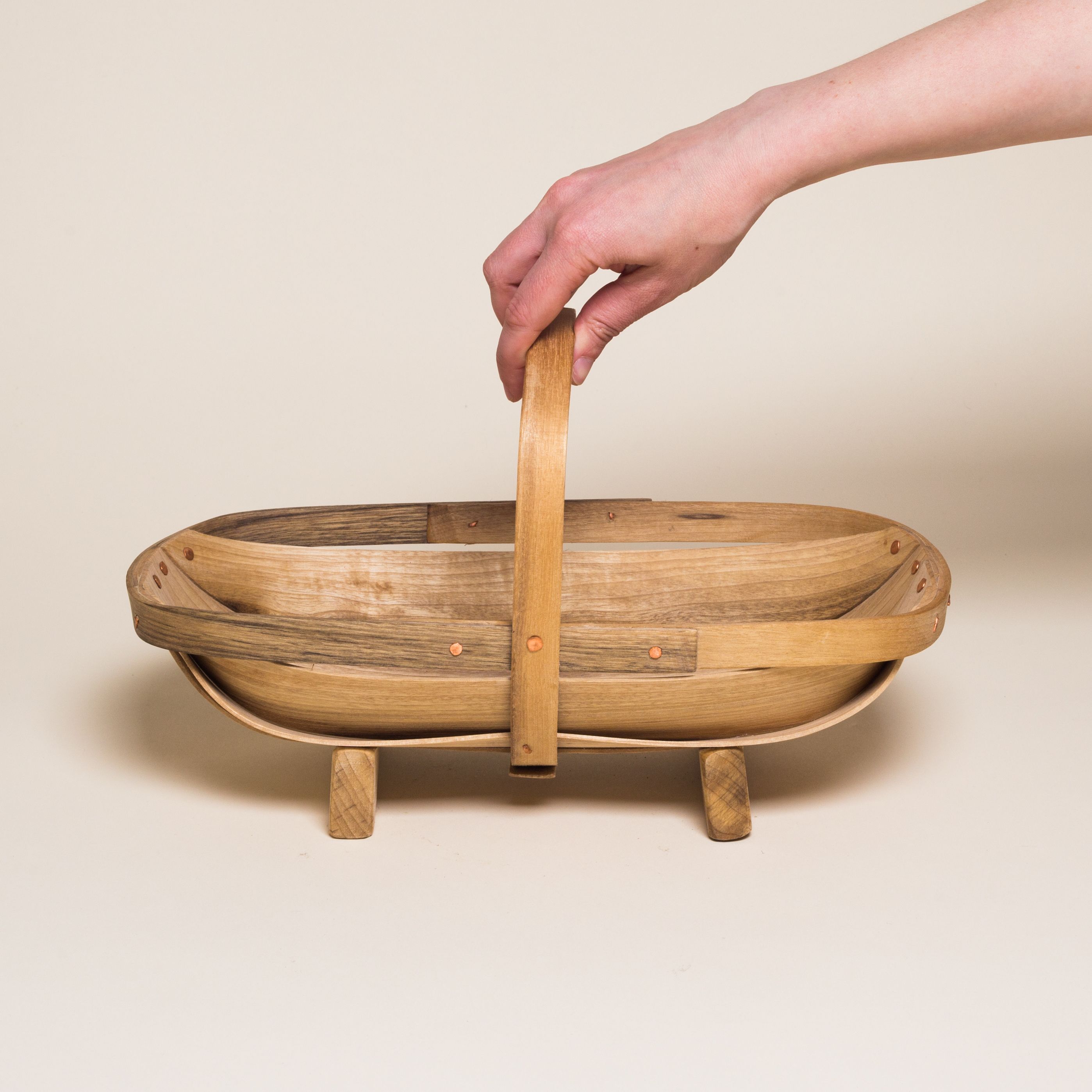 A wooden trug basket with two feet and a handle that encircles the center