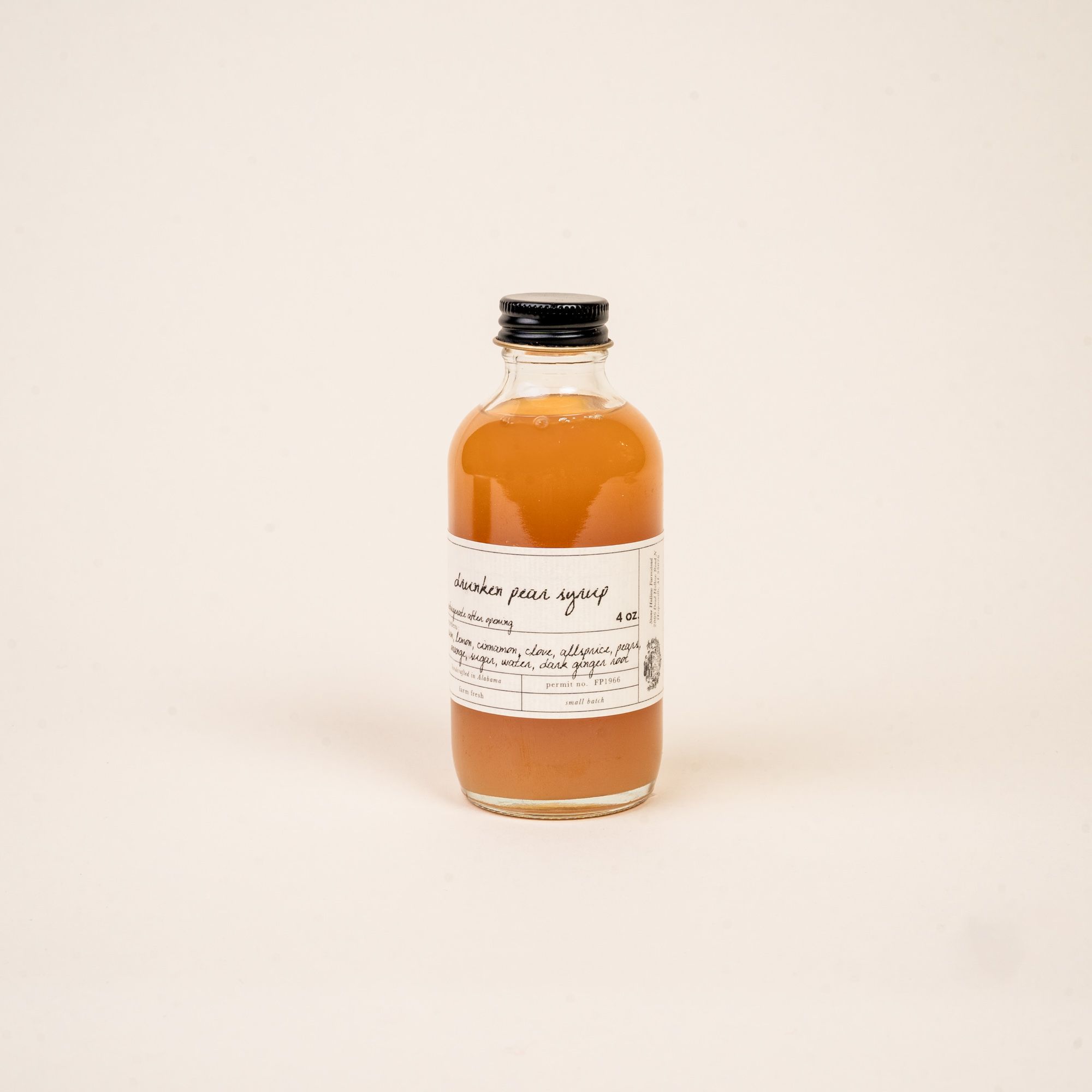 A short narrow bottle with a black top with syrup inside and a label that reads 'Drunken Pear Syrup'