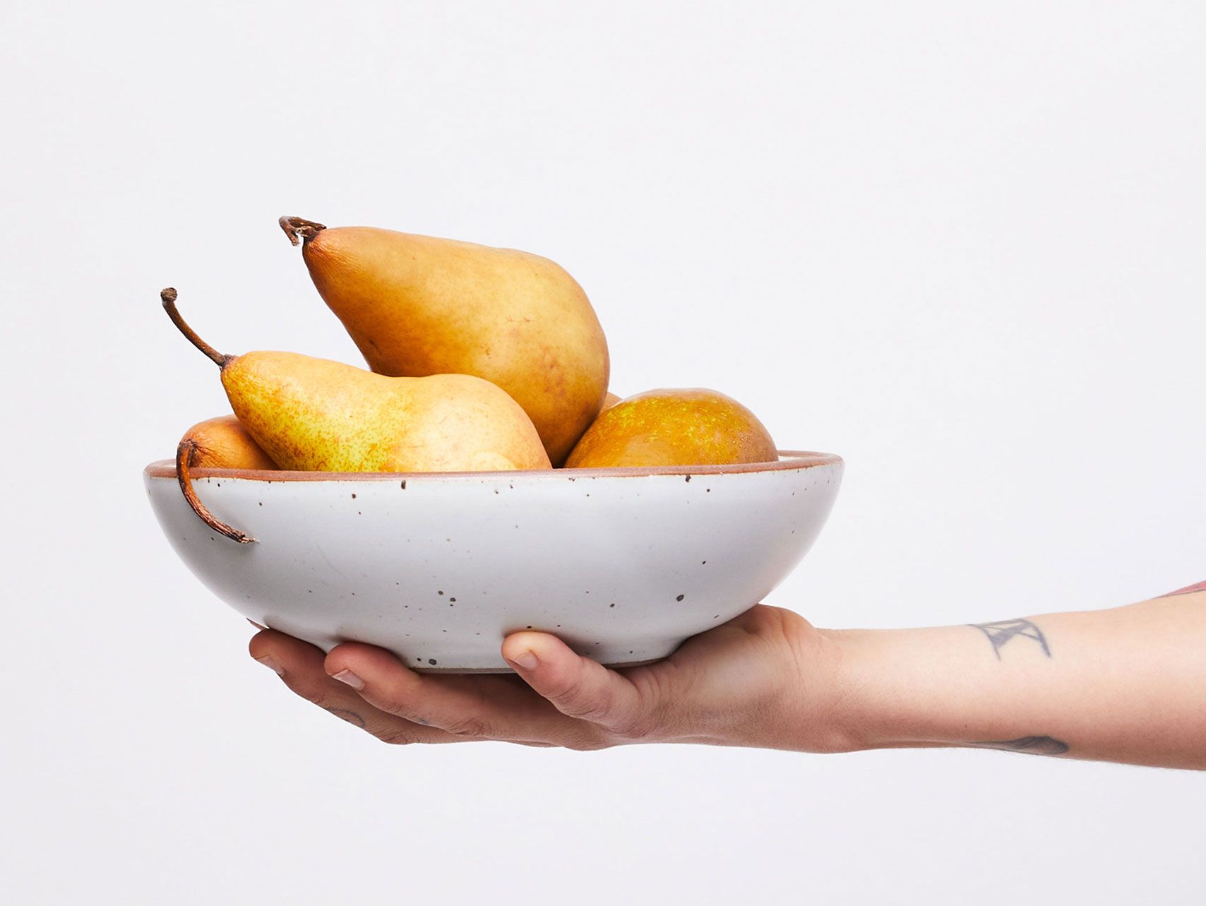 A hand holding an eggshell everyday bowl filled with pears