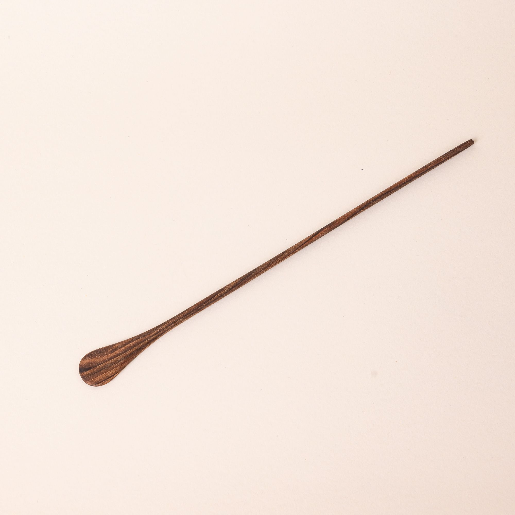 A long thin walnut cocktail stirrer with a small spoon-like shape on the end