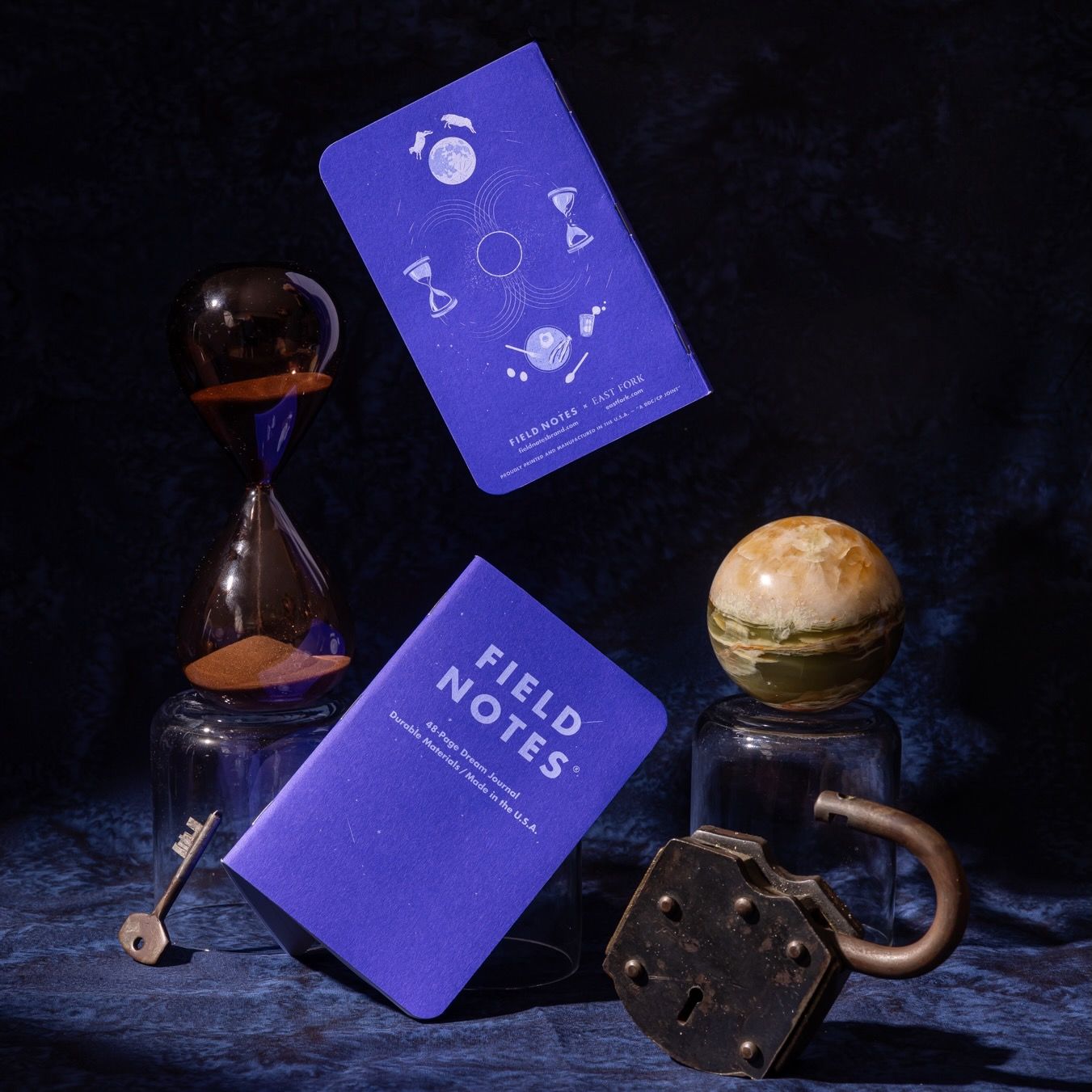 An artful photo featuring the Field Notes dream journal in a lapis blue with moons and time motifs illustrated on the back cover, and like products surrounding the journals.