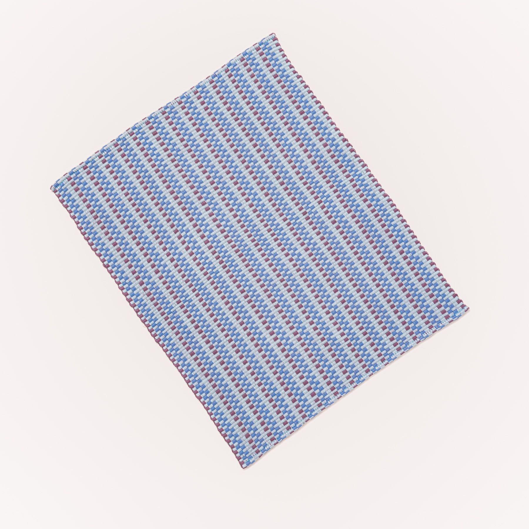 A woven placemat with thin horizontal striped tonal soft blue and purple colors