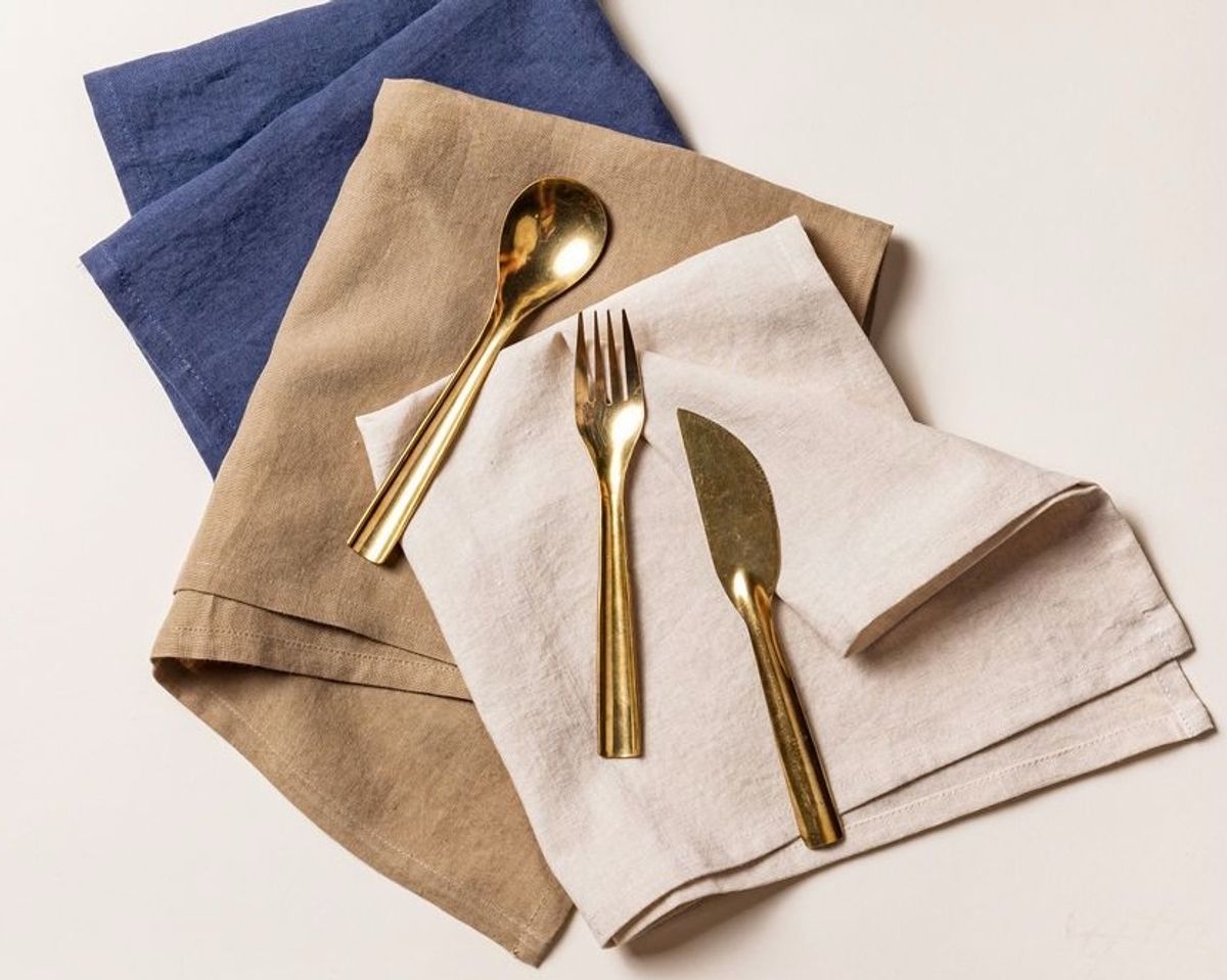 A table setting with a neutral woven placemat, stacked cool white ceramic plates, and ivory marble-handled fork, knife, and spoon.