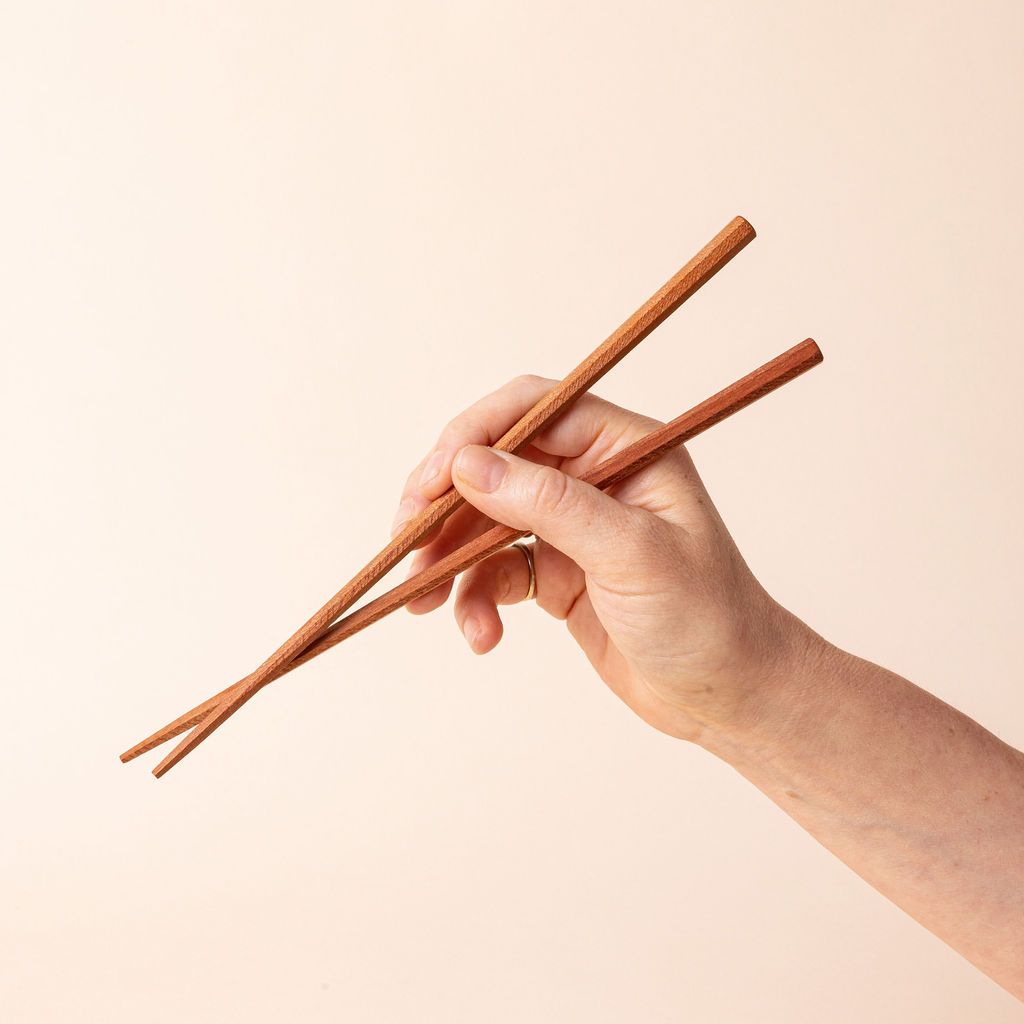 A hand holding simple light brown wood chopsticks