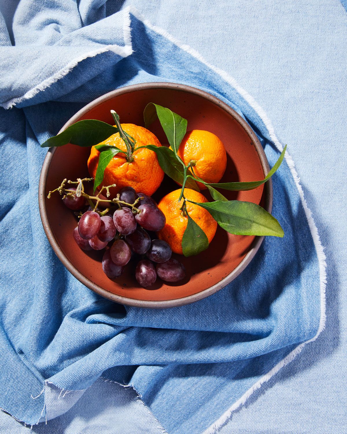 Oranges and grapes in an Amaro bowl on a light blue towel