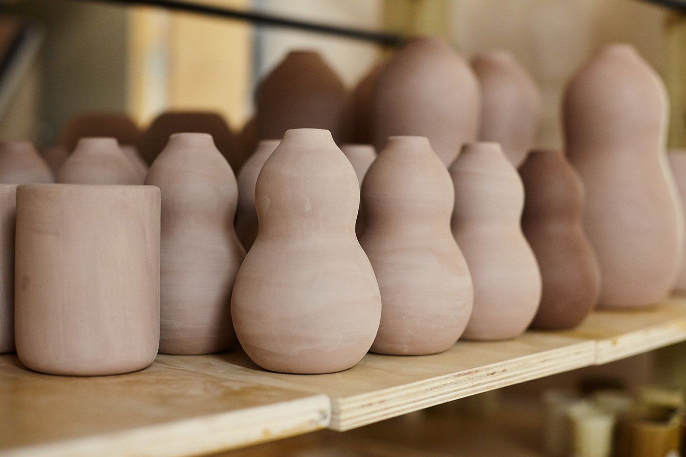 A shelf holds ceramic bisqueware, including curvy vases, and utensil holders.