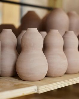 A shelf holds ceramic bisqueware, including curvy vases, and utensil holders.