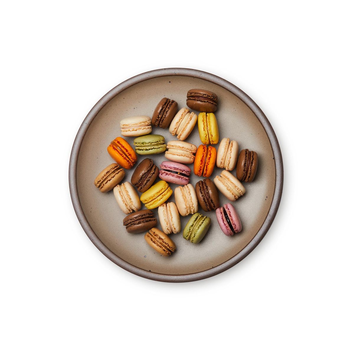 Macarons on a dinner sized ceramic plate in a warm pale brown color featuring iron speckles and an unglazed rim.