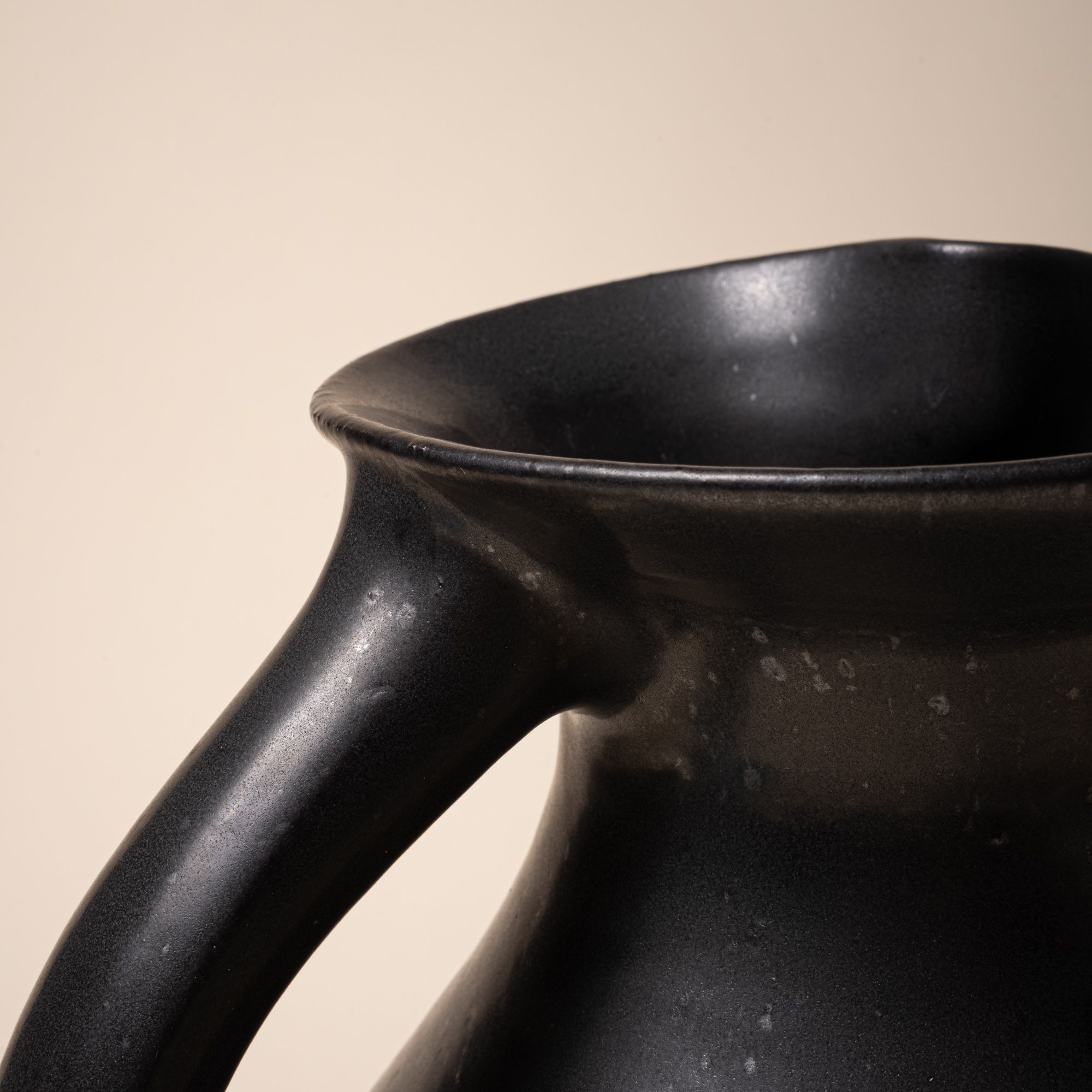 A closeup of the top of the handle connected to the top of a ceramic pitcher.