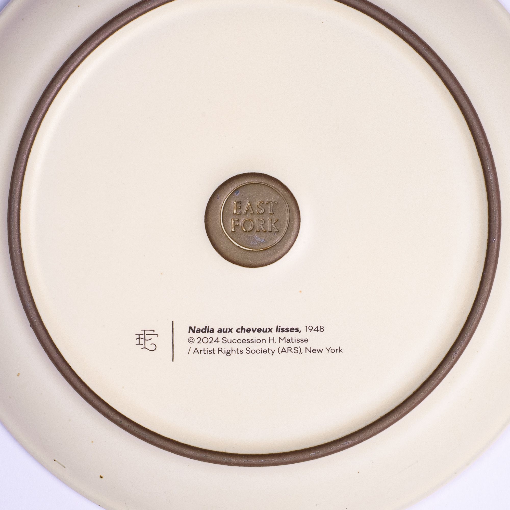 The back of a side plate with an East Fork stamp with a small decal of information about the artwork, Nadia aux cheveux lisses, by Henri Matisse.