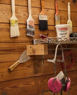 Some tools hang on the wall of woodworking workshop, including wide paint brushes, a mask, and more