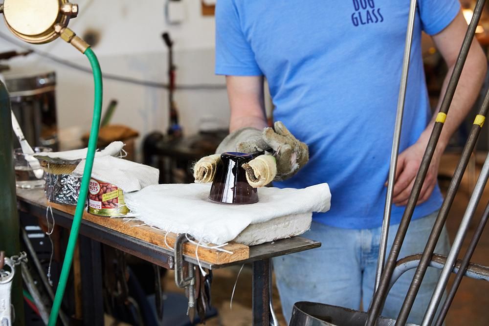 In a workshop setting, a person holds a glass upside down with special tools on a piece of fabric