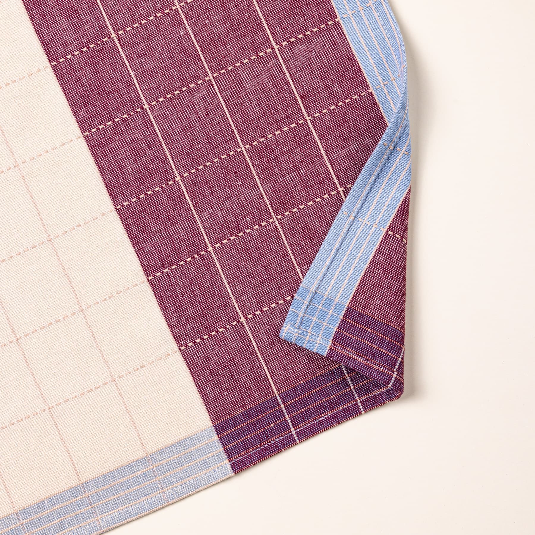 A look at a corner of a flat plaid napkin in plum and periwinkle colors with white gridlines.