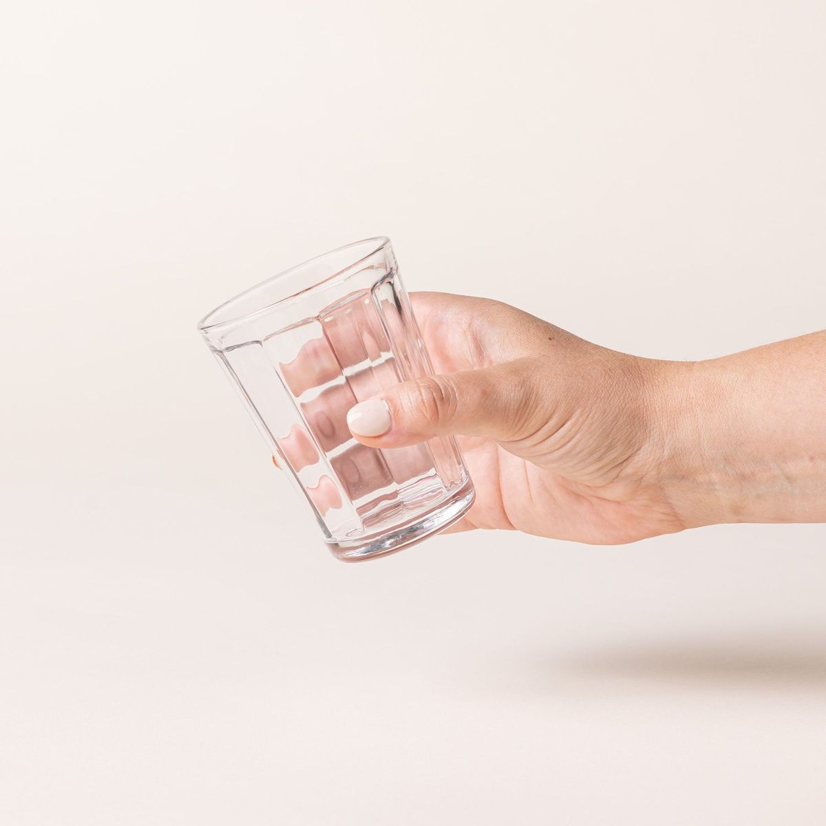 A hand holds a medium diner-style glass that tapers to be wider at the top