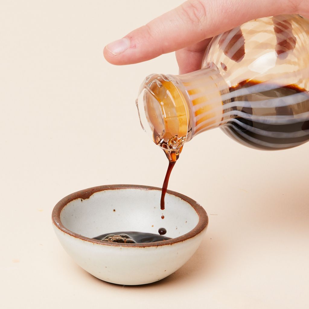 Eggshell Bitty Bowl with stream of dark brown soy sauce poured by a hand from a glass cruet